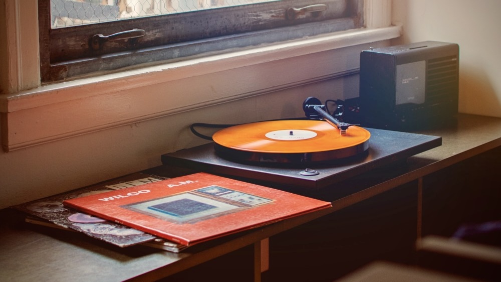 Record player playing orange vinyl record in vintage room under the window.